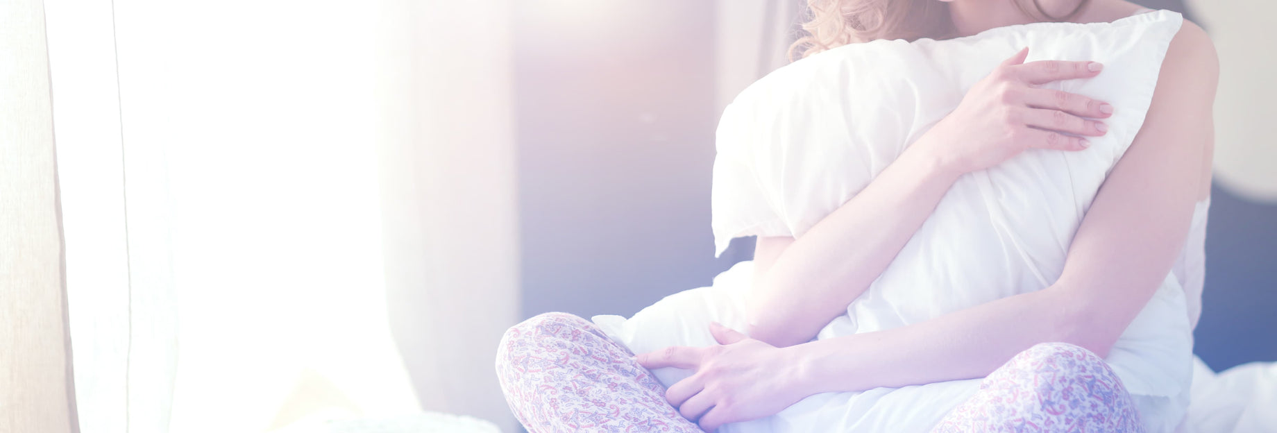 Woman sitting on bed and hugging a pillow in the morning