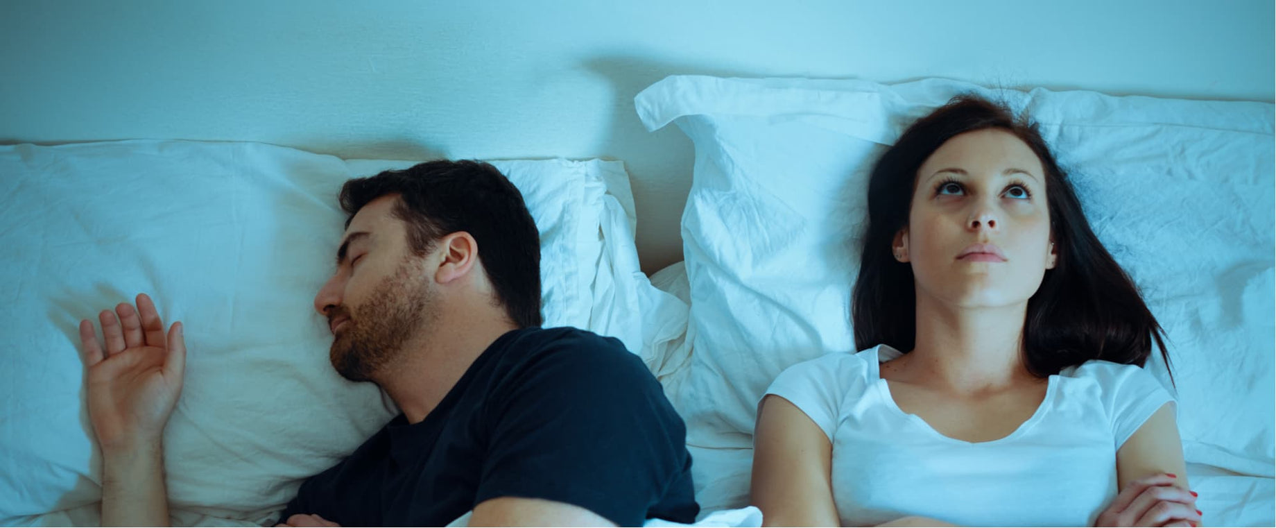 Woman experiencing sleep issues, laying next to man in bed