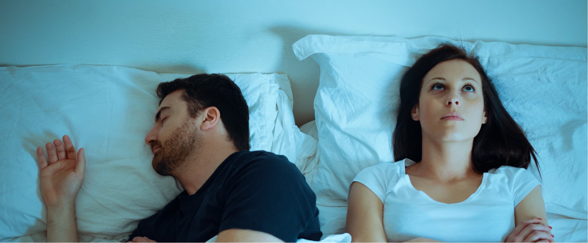Woman experiencing sleep issues, laying next to man in bed