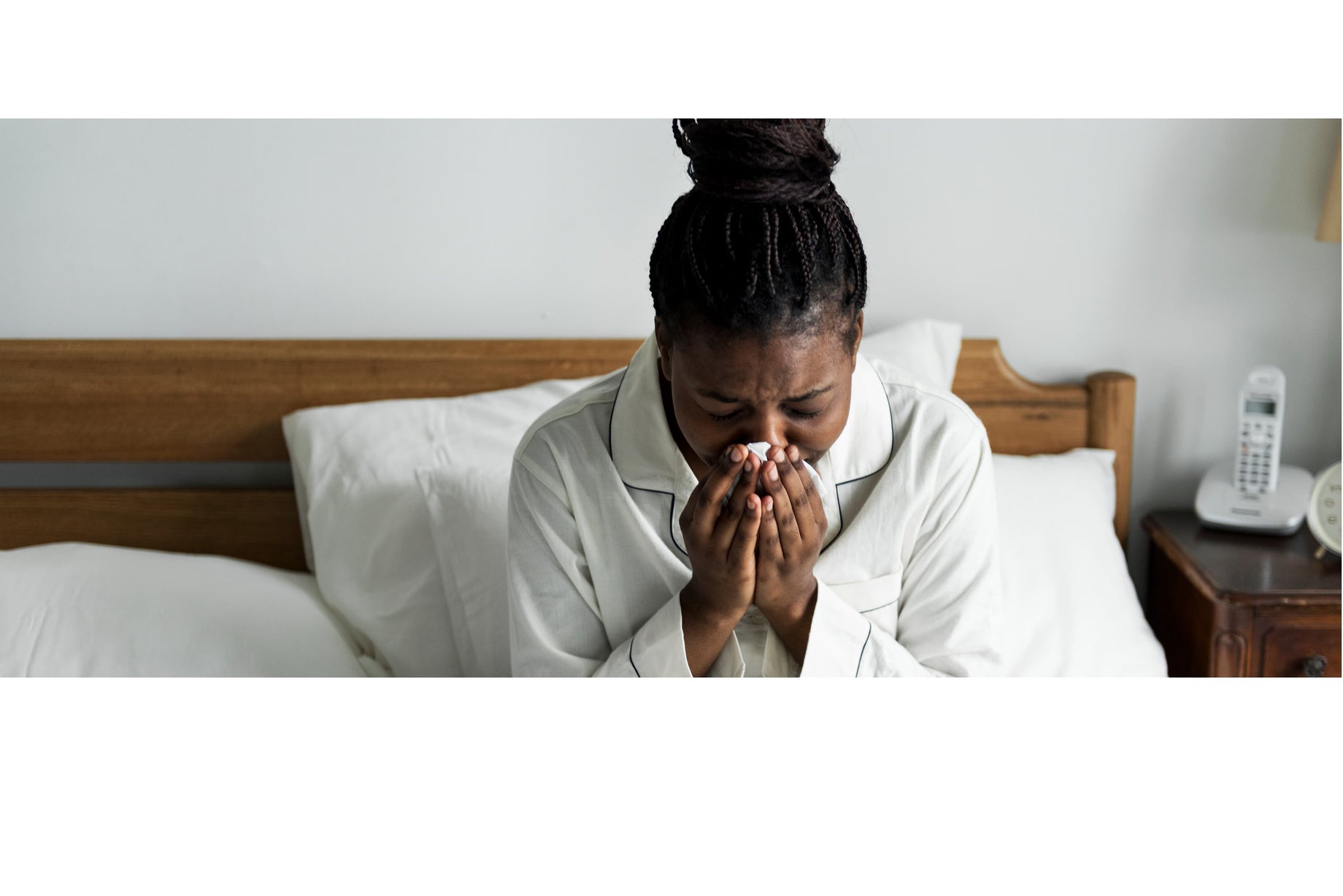 Woman blowing her nose in bed because of allergies